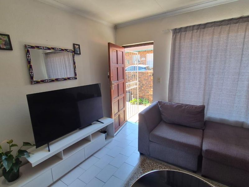 A living room area featuring tiled flooring and direct access to the exterior through a timber door with a security gate.