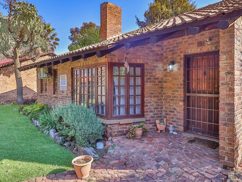 A charming townhouse exterior featuring exposed brickwork, a classic bay window, a brick chimney, and a paved patio area overlooking a well-maintained garden.