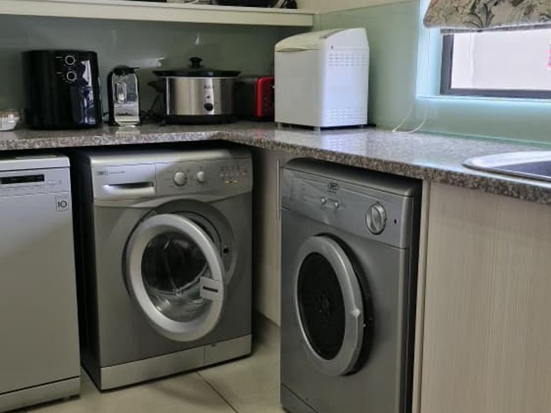 A functional laundry area featuring tiled flooring, granite countertops, a stainless steel sink, and built-in cabinetry with a glass splashback.