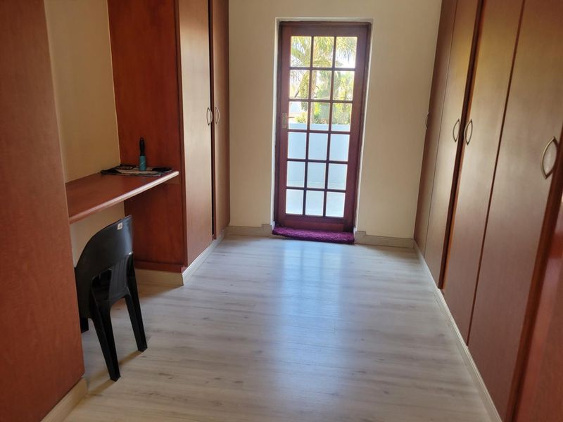 A bedroom featuring extensive built-in cabinetry, a built-in desk, light laminate flooring, and a glass-paneled door providing access to the exterior.