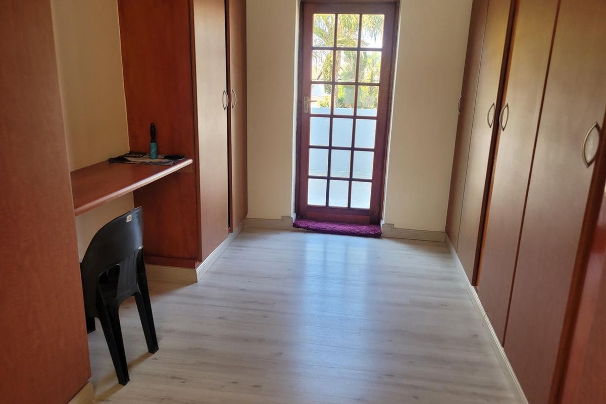 A bedroom featuring extensive built-in cabinetry, a built-in desk, light laminate flooring, and a glass-paneled door providing access to the exterior.