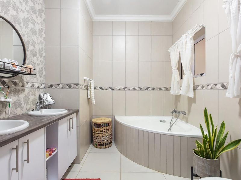 A well-maintained bathroom featuring a double vanity with built-in cabinetry, tiled walls, and a corner bathtub with a mixer tap.