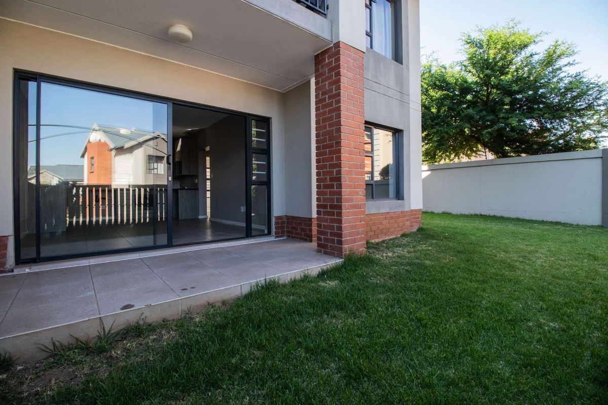 A private rear patio featuring tiled flooring and a brick pillar, providing seamless access to the open-plan interior and the adjacent garden area.