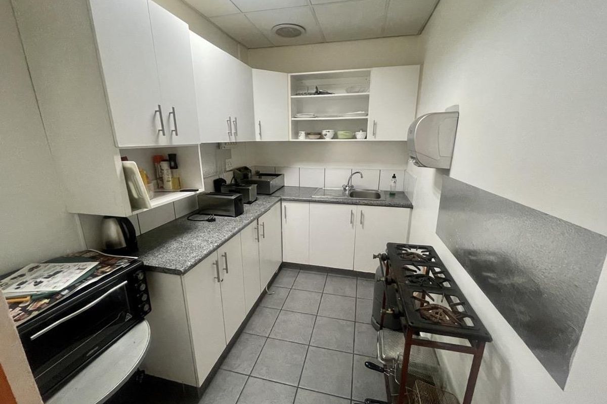 Compact industrial kitchenette featuring white cabinetry, granite-look laminate countertops, stainless steel sink, and tiled flooring.