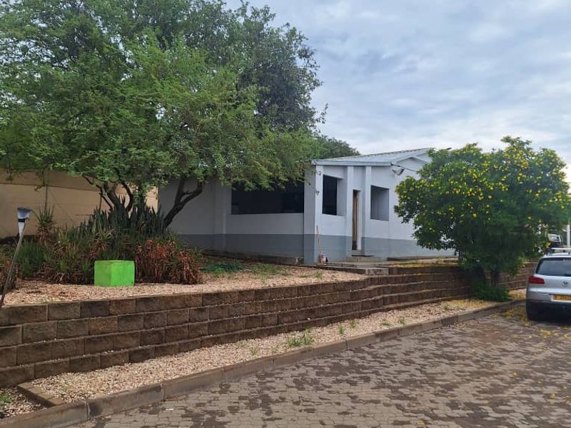 Front exterior view of the industrial property featuring a paved driveway, retaining wall, and established garden area.