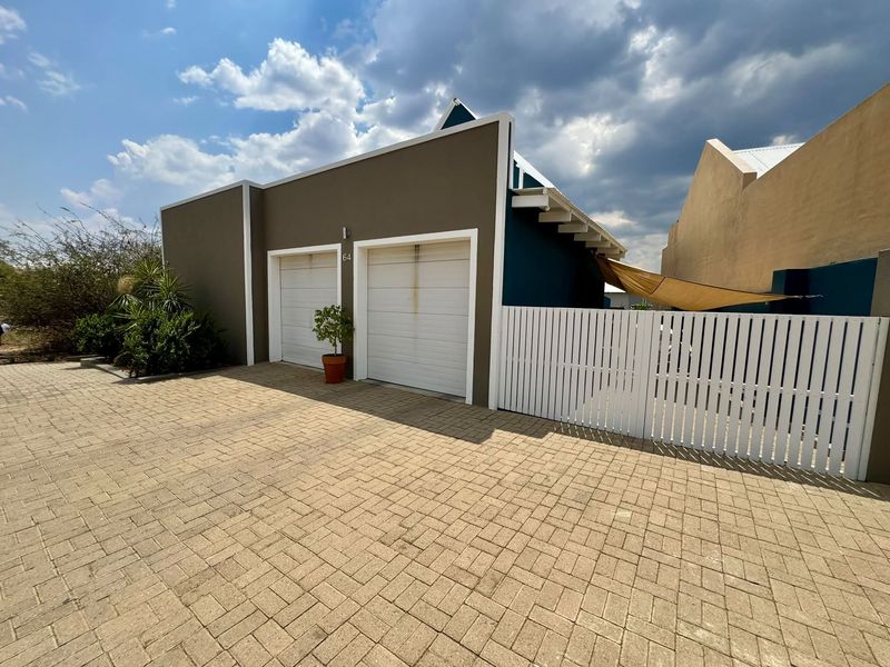 Front exterior view of the property featuring a double garage with paved driveway and a white picket fence.