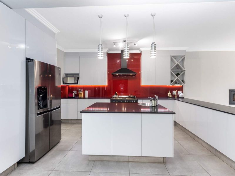 Modern kitchen featuring a central island, sleek white cabinetry, contrasting dark countertops, a striking red glass splashback, and integrated appliances.