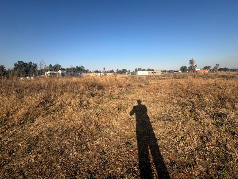 A wide-angle view of a vacant residential plot featuring dry grass and open terrain, suitable for future development.