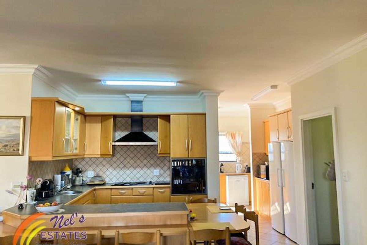 A functional kitchen featuring light wood cabinetry, a built-in oven, extractor fan, and a breakfast bar, with an adjacent scullery area.