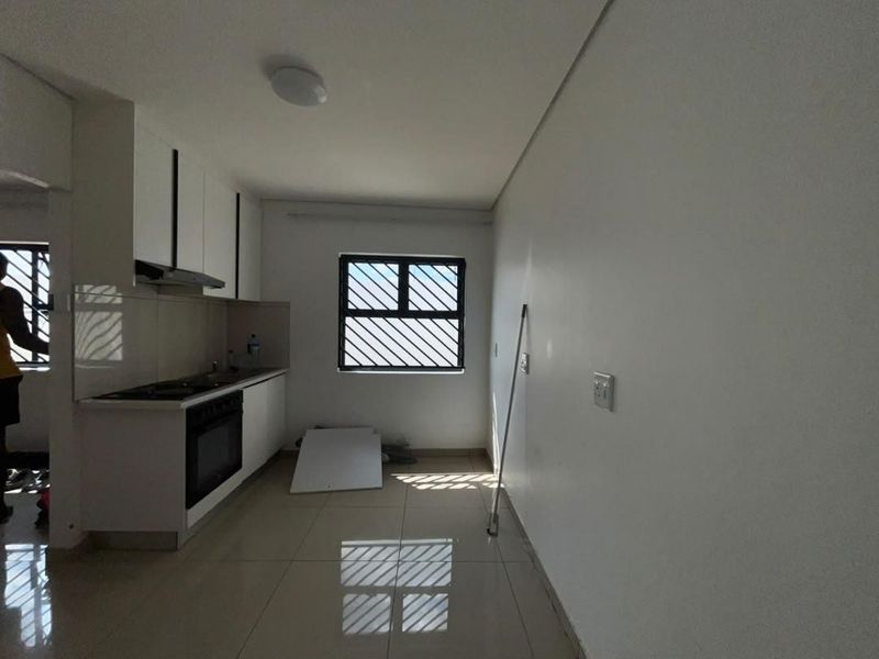 A clean, empty kitchen featuring modern white cabinetry, built-in oven, hob, extractor fan, and tiled flooring with security bars on the window.