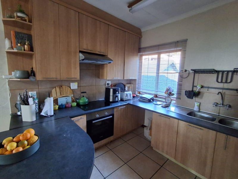 Functional kitchen featuring wood-look laminate cabinetry, dark countertops, built-in oven with hob, extractor fan, and double stainless steel sink with tiled backsplash.