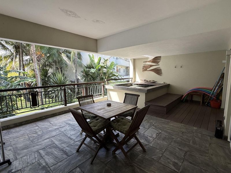Spacious covered balcony featuring stone tile flooring, a built-in plunge pool, timber decking, and a metal balustrade overlooking lush tropical garden views.