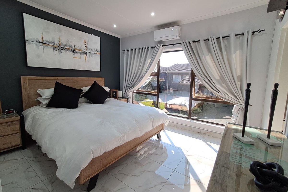 A well-lit bedroom featuring large windows, tiled flooring, and a wall-mounted air conditioning unit, offering a bright and comfortable living space.