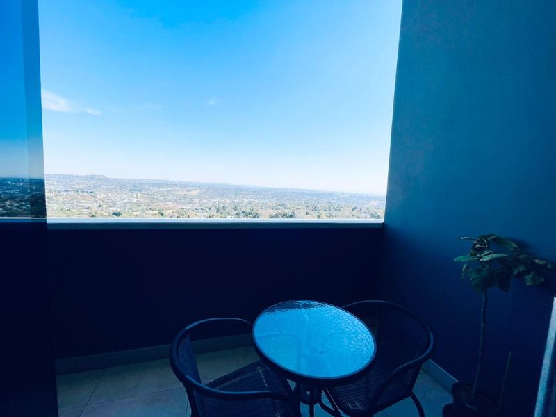 A private balcony featuring tiled flooring and a glass balustrade, offering expansive elevated views of the surrounding landscape.