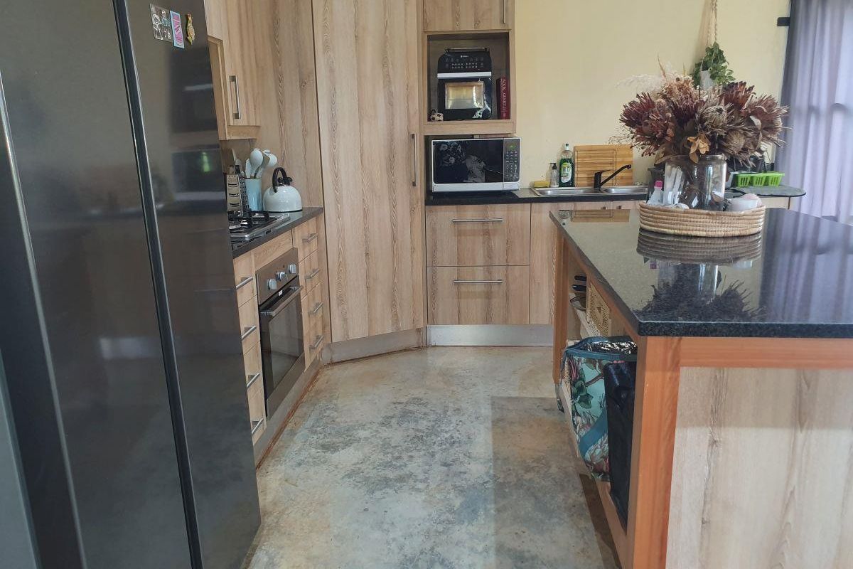 Modern kitchen featuring light wood cabinetry, granite countertops, a central island, and polished concrete flooring with integrated oven and hob.