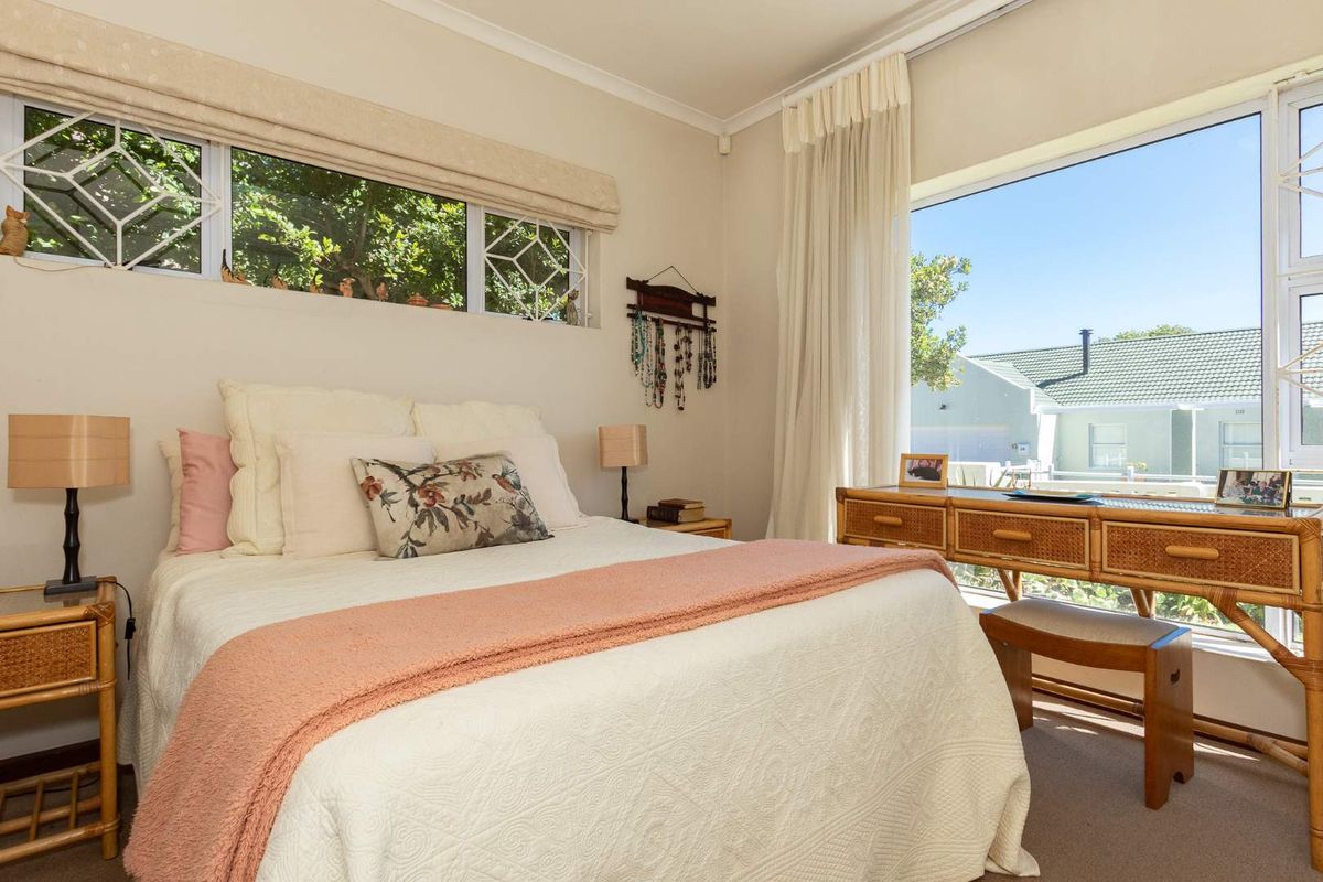 A bright bedroom featuring large windows with security bars, neutral carpeting, and classic cornice detailing.