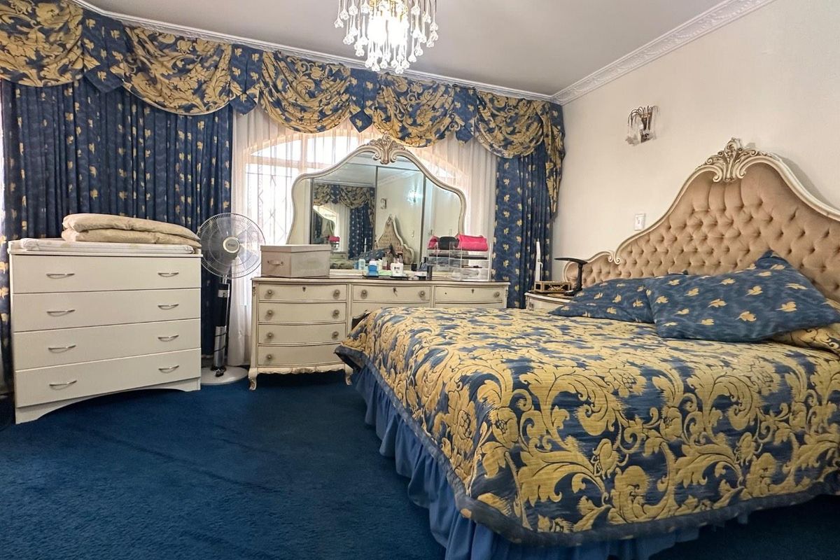 A spacious bedroom featuring ornate crown molding, a decorative chandelier, and wall-to-wall carpeting.