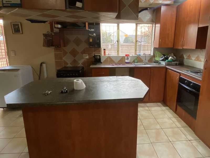A functional kitchen featuring wooden cabinetry, a central island, tiled backsplash, and built-in oven, offering a practical layout with potential for modern updates.