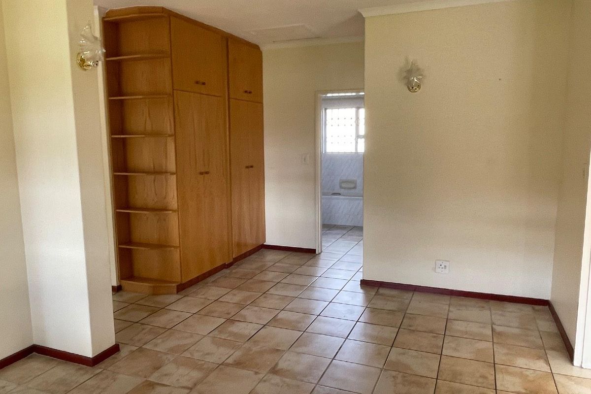 An empty bedroom featuring built-in wooden cupboards, tiled flooring, and direct access to an en-suite bathroom.