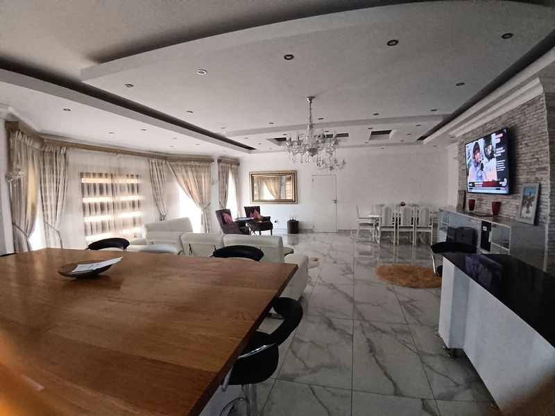 Spacious open-plan living and dining area featuring high-gloss marble-look flooring, a modern recessed ceiling with downlights, and a striking stone feature wall.