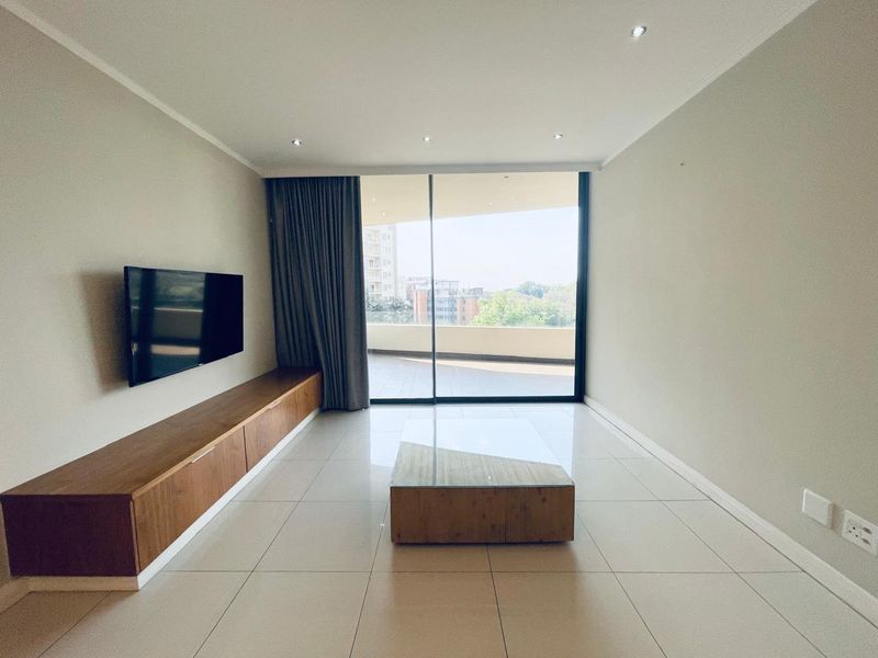 Modern living room featuring tiled floors, recessed lighting, and a built-in wooden media console, with direct access to a spacious balcony through sliding glass doors.