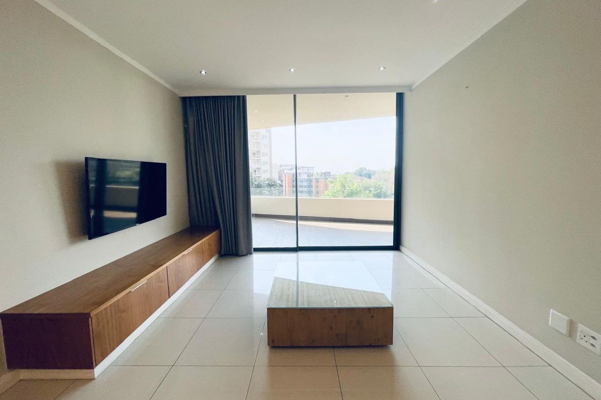 Modern living room featuring tiled floors, recessed lighting, and a built-in wooden media console, with direct access to a spacious balcony through sliding glass doors.