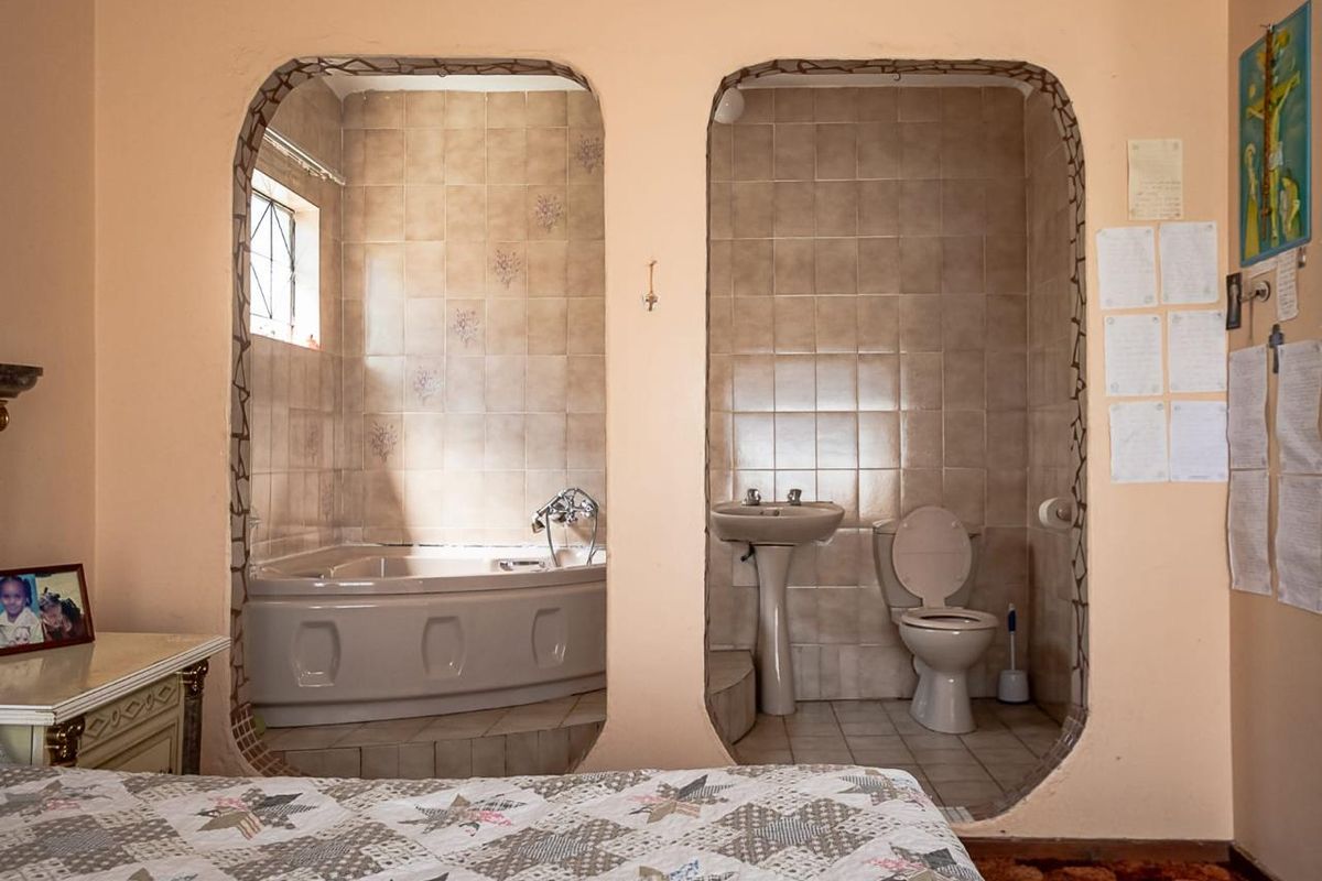 En-suite bathroom featuring a corner bathtub, pedestal sink, and toilet, separated from the bedroom by distinctive arched openings with tiled finishes.