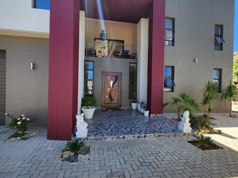 Modern double-story house entrance featuring a bold burgundy portico, paved driveway, and a balcony overlooking the front facade.
