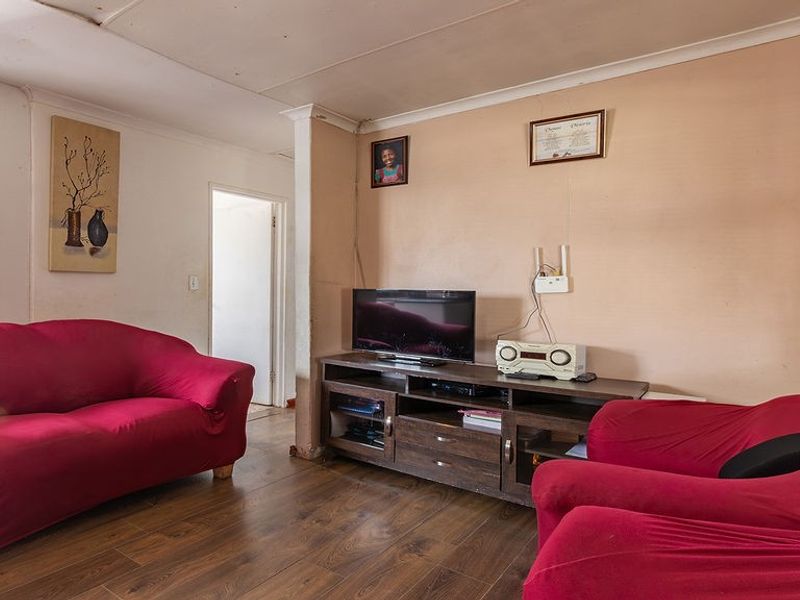 A living room featuring laminate flooring and coved ceilings, currently showing signs of wear and requiring cosmetic updates to improve its overall condition.