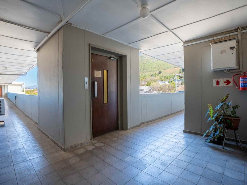A covered apartment building hallway featuring tiled flooring, an elevator access point, and essential fire safety equipment.