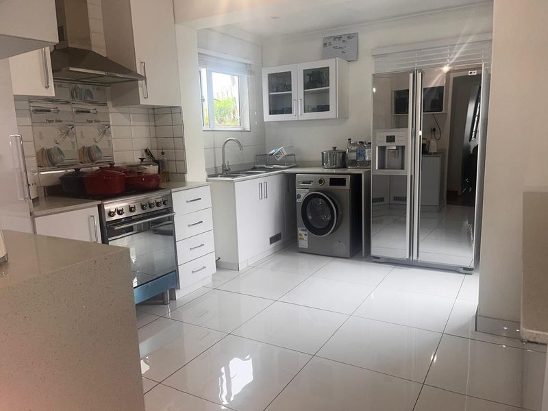 Modern kitchen featuring white cabinetry, quartz countertops, stainless steel appliances, and polished tiled flooring with an integrated laundry area.