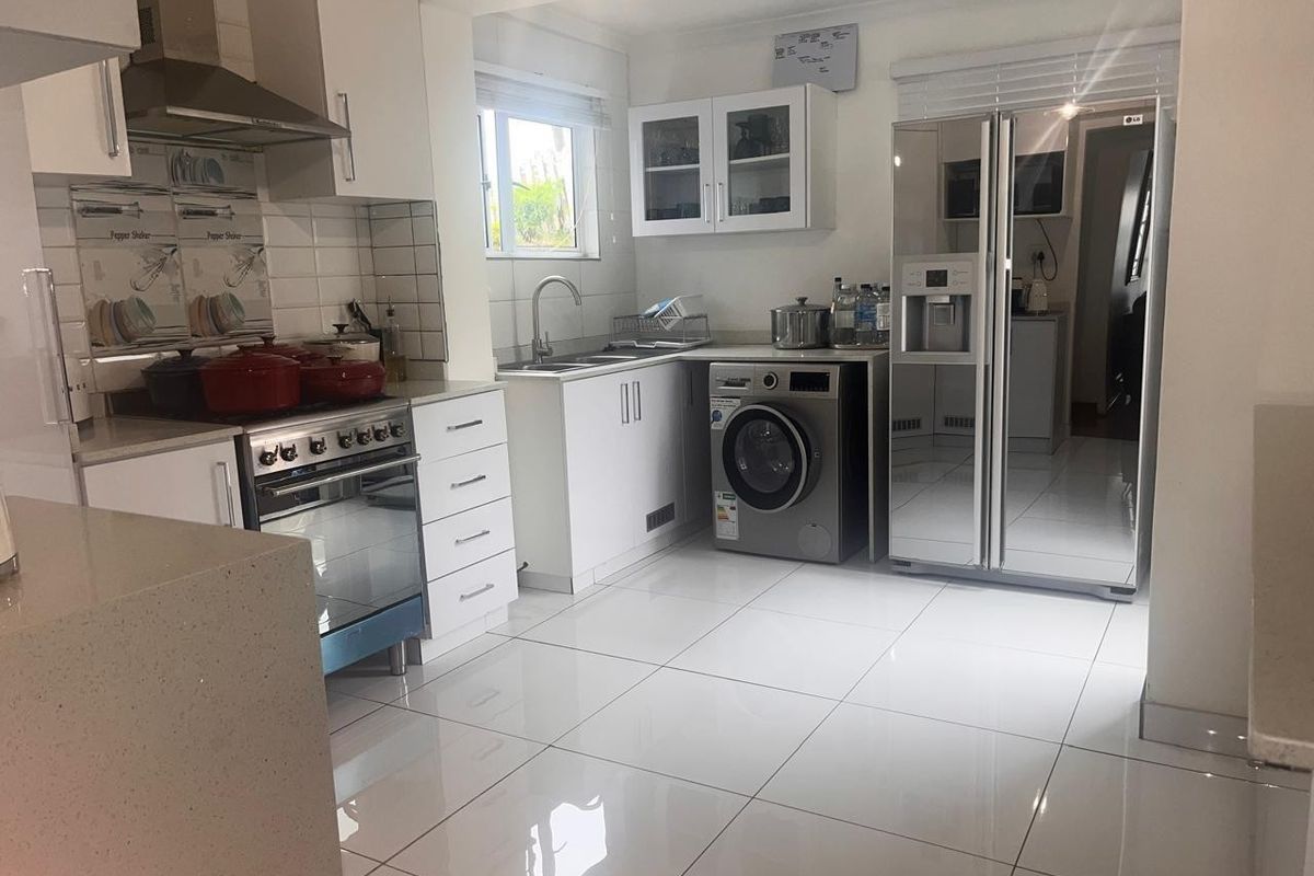 Modern kitchen featuring white cabinetry, quartz countertops, stainless steel appliances, and polished tiled flooring with an integrated laundry area.