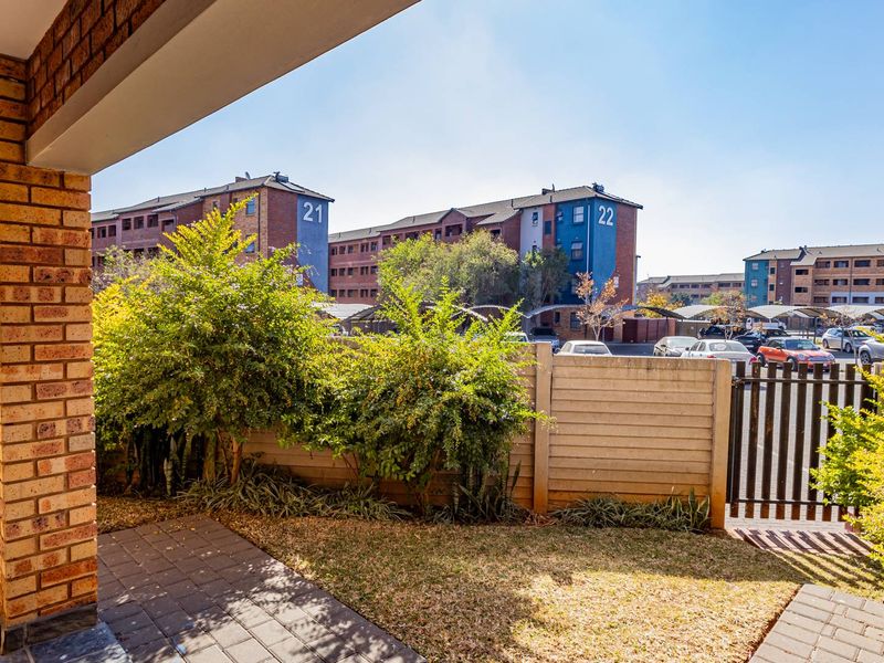 A private paved patio area featuring a brick pillar, precast concrete boundary wall, and metal gate, overlooking the apartment complex grounds.