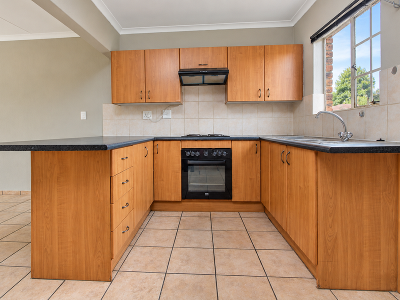A functional U-shaped kitchen featuring wood-look cabinetry, built-in oven, electric hob, and tiled finishes, offering a clean and practical workspace.