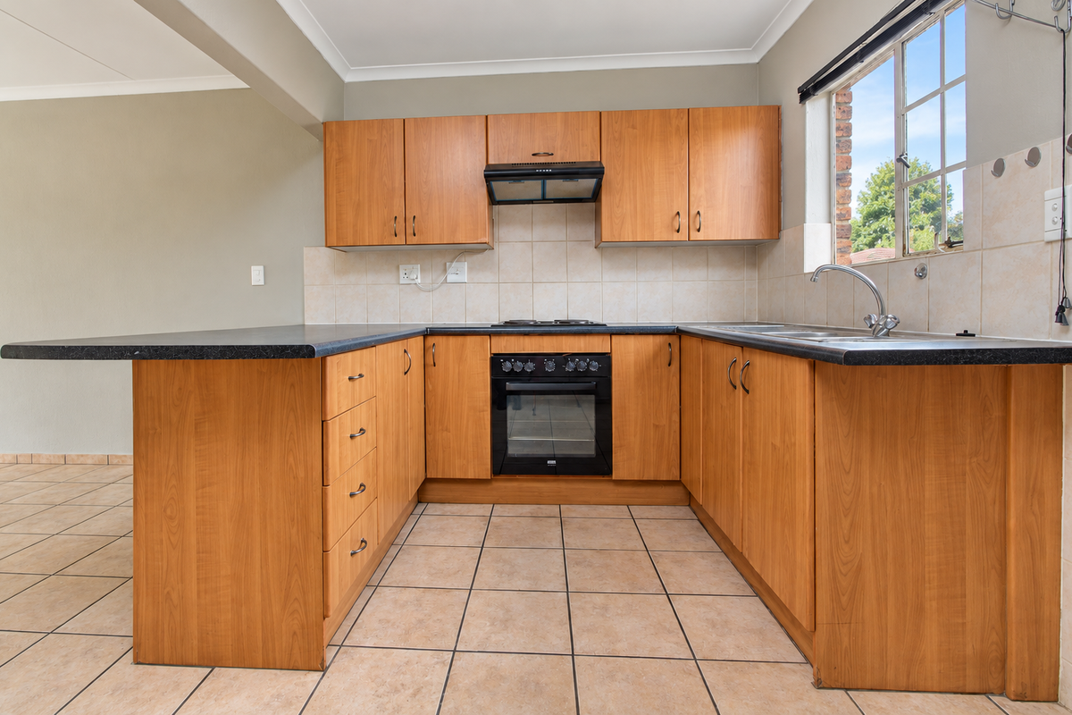 A functional U-shaped kitchen featuring wood-look cabinetry, built-in oven, electric hob, and tiled finishes, offering a clean and practical workspace.