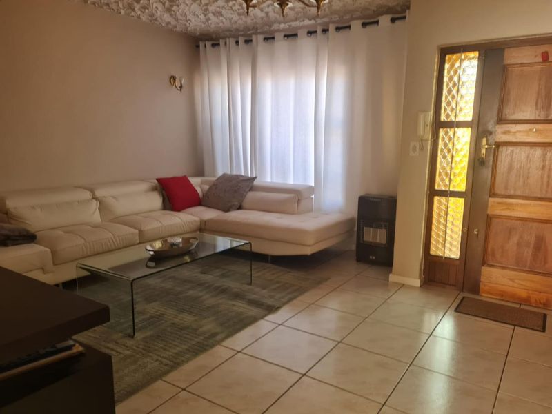 A living room featuring tiled flooring, a textured ceiling, and a wooden front door with decorative glass panels.