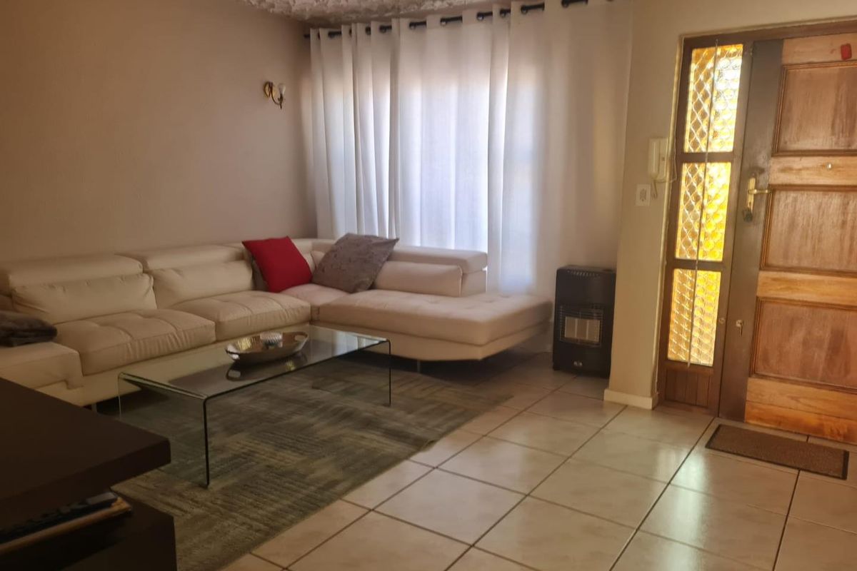 A living room featuring tiled flooring, a textured ceiling, and a wooden front door with decorative glass panels.
