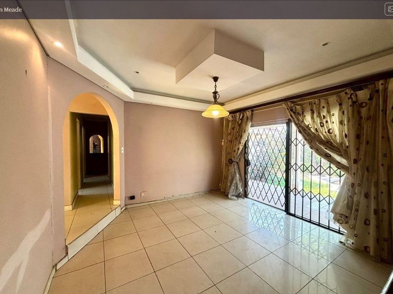 An empty living room featuring tiled flooring, a decorative recessed ceiling, and a sliding glass door with a security gate leading to the exterior.