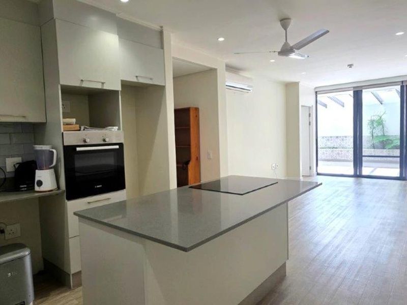 Spacious open-plan kitchen and living area featuring a central island, built-in oven, hob, and seamless access to an outdoor patio through large sliding doors.