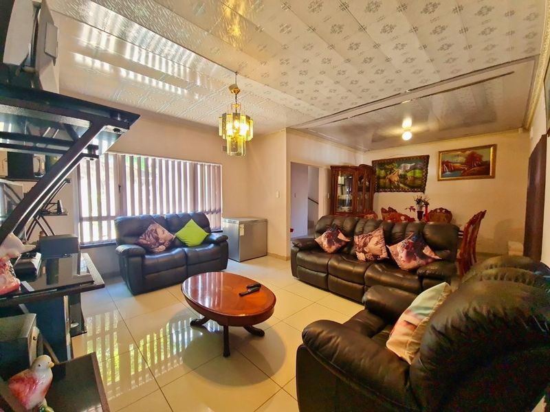Spacious open-plan living and dining area featuring tiled flooring, decorative ceiling tiles, and large windows with vertical blinds.