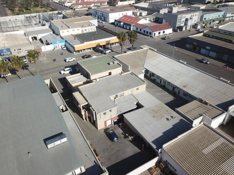 Aerial view of a mixed-use commercial property featuring multiple buildings with corrugated metal roofing and an asphalt parking area.