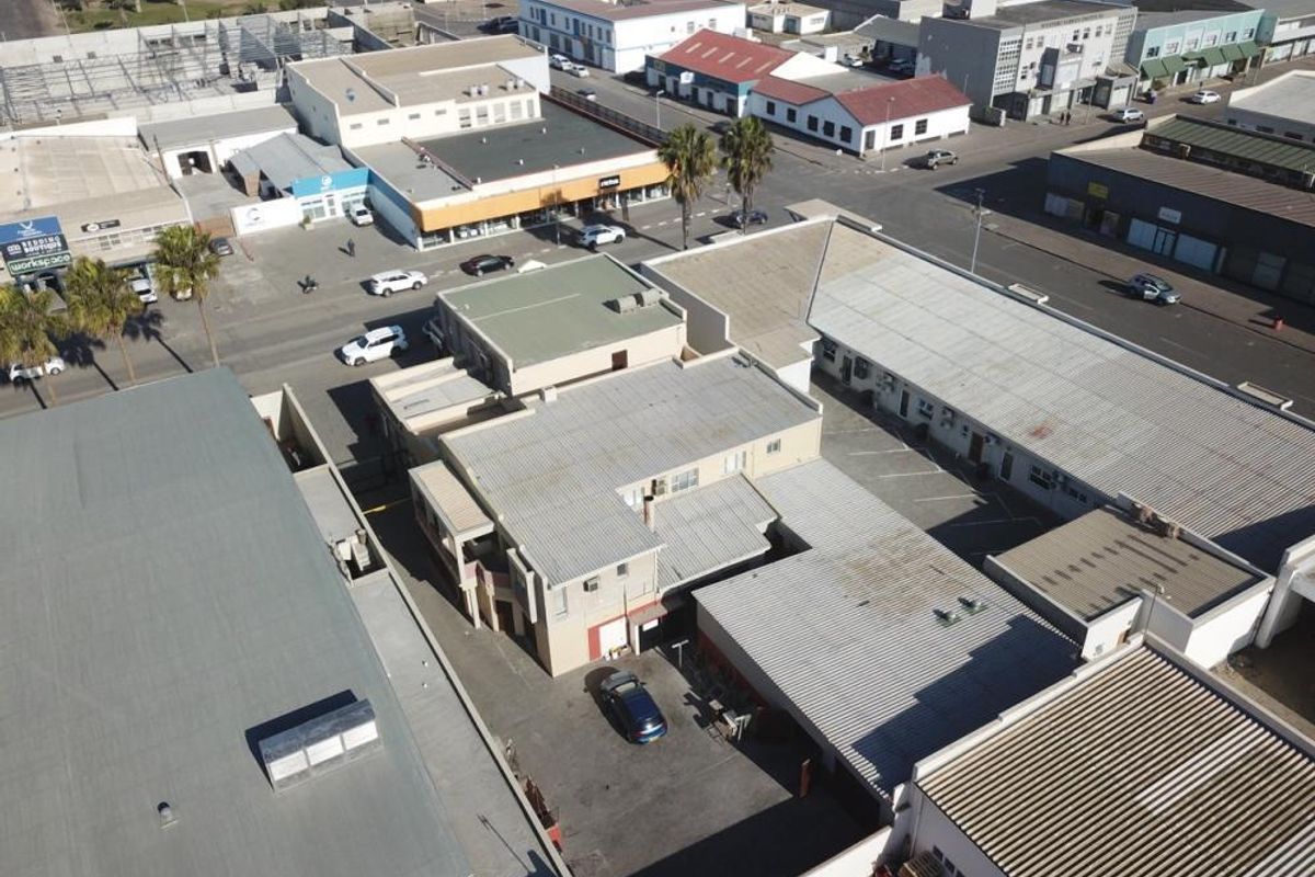 Aerial view of a mixed-use commercial property featuring multiple buildings with corrugated metal roofing and an asphalt parking area.