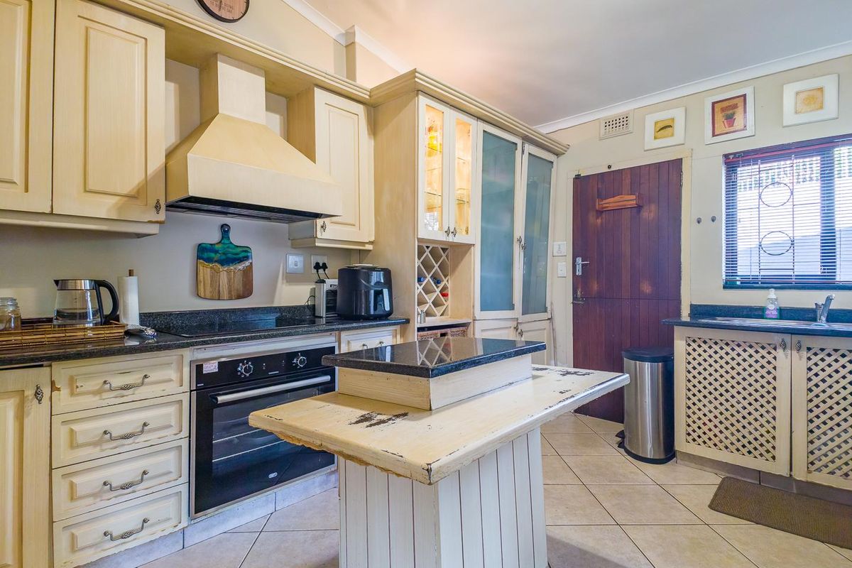 A traditional kitchen featuring cream-colored cabinetry, granite countertops, a built-in oven with extractor fan, and a central island with a worn finish.