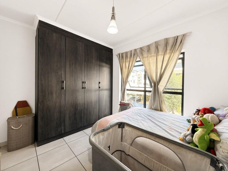 A well-lit bedroom featuring dark wood built-in cupboards, tiled flooring, and a large window with natural light.