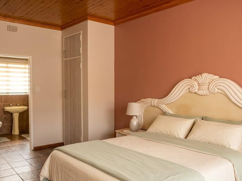 A bedroom featuring a wooden ceiling, built-in cupboard, and an en-suite bathroom with tiled flooring and a pedestal sink.