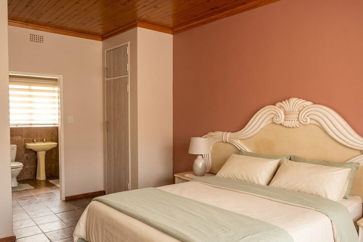 A bedroom featuring a wooden ceiling, built-in cupboard, and an en-suite bathroom with tiled flooring and a pedestal sink.
