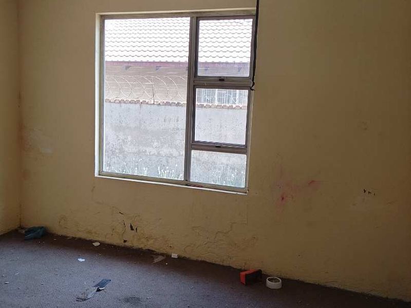 An empty bedroom featuring carpet flooring and an aluminium window frame, currently requiring cosmetic repairs and wall surface restoration.