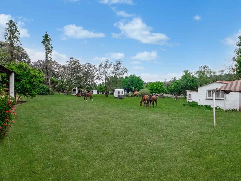 Expansive green lawn area on a farm property featuring mature trees, an outbuilding, and a covered patio space.