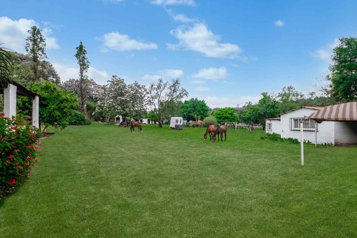 Expansive green lawn area on a farm property featuring mature trees, an outbuilding, and a covered patio space.
