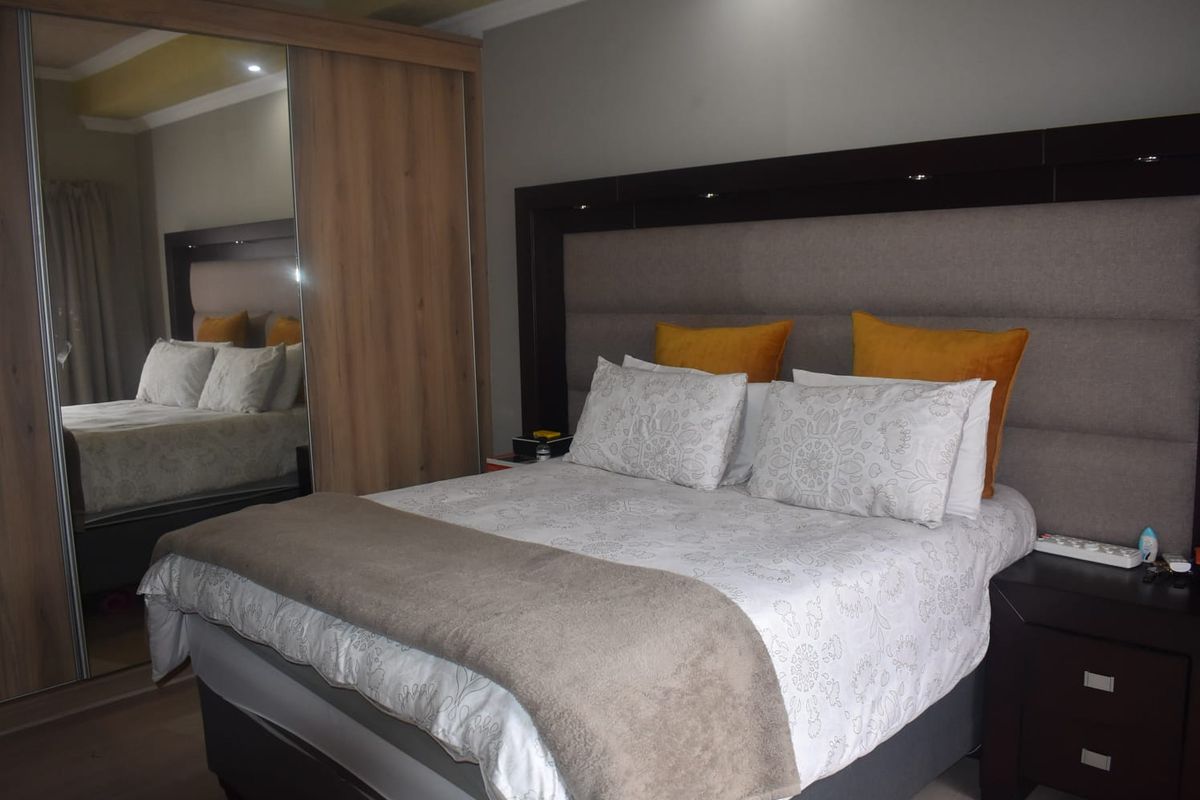 A well-maintained bedroom featuring a large built-in wardrobe with mirrored sliding doors and a modern upholstered headboard.